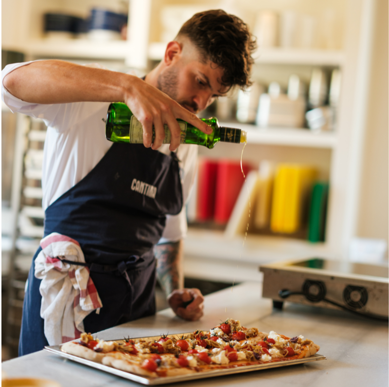 Chef pouring olive oil on a dish in the Cantina kitchen